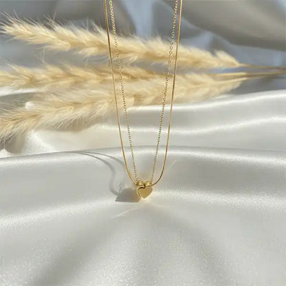 Gold double chain heart pendant necklace displayed on white satin fabric with soft sunlight and pampas grass, anti-tarnish jewellery
