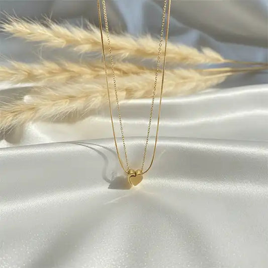 Gold double chain heart pendant necklace displayed on white satin fabric with soft sunlight and pampas grass, anti-tarnish jewellery