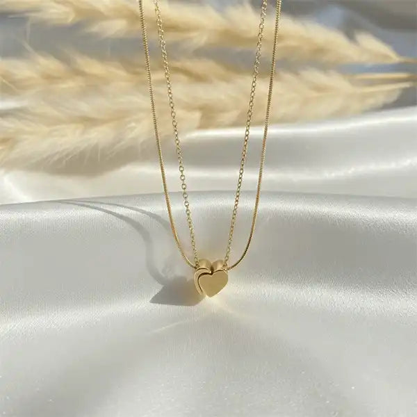 Minimal gold heart pendant with double chain resting on white satin cloth, anti-tarnish everyday jewellery, premium