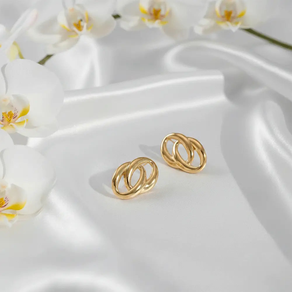 K-A Trends anti tarnish gold double loop stud earrings on white silk fabric with orchid flowers luxury product shoot