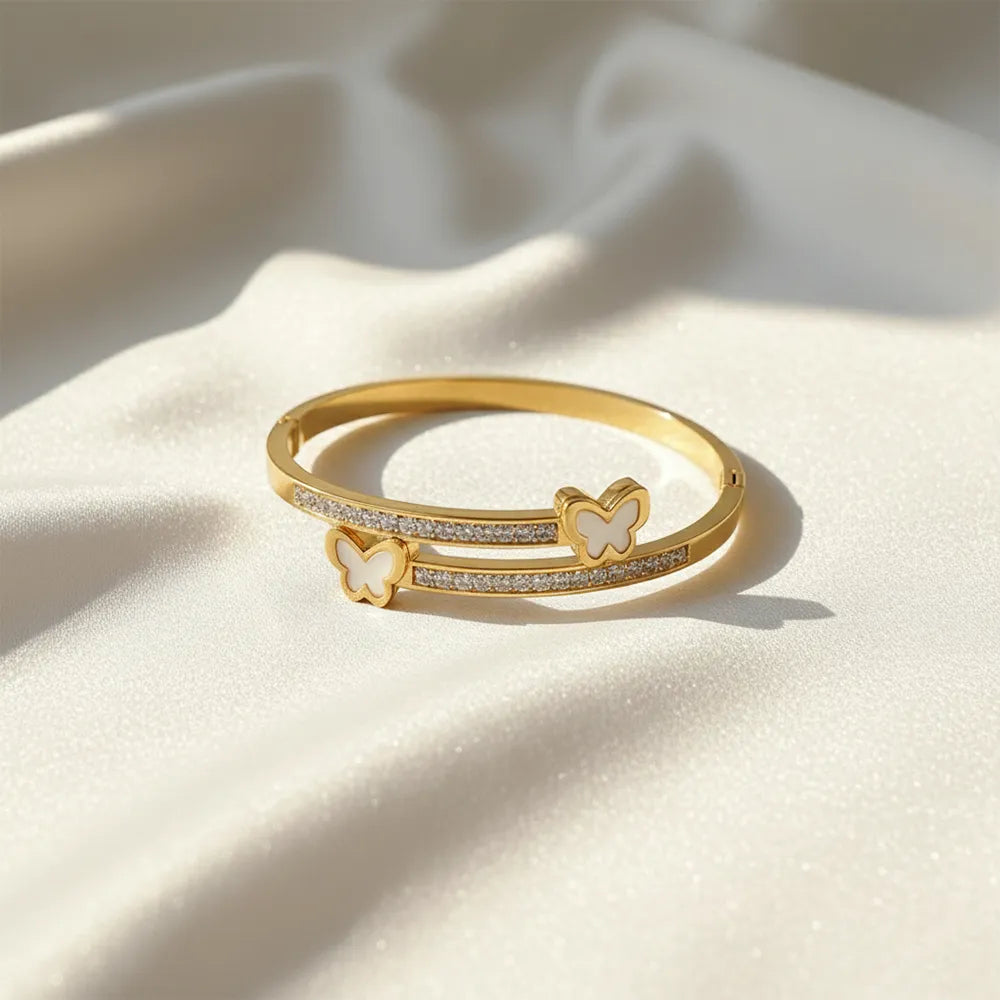 Gold bracelet with butterfly charms and crystal details on a satin cloth.