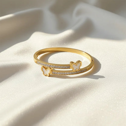 Gold bracelet with butterfly charms and crystal details on a satin cloth.