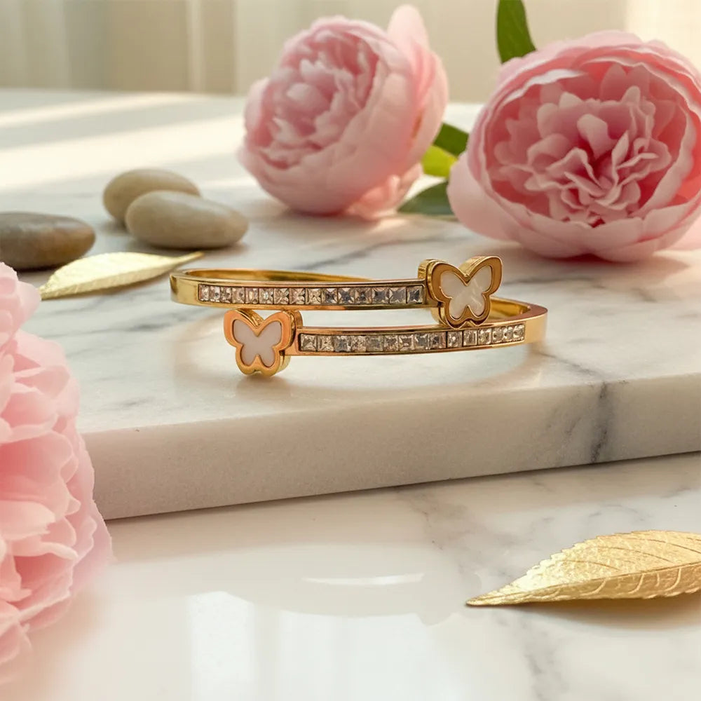 Gold bracelet with butterfly charms and crystal details on a marble surface with pink flowers.