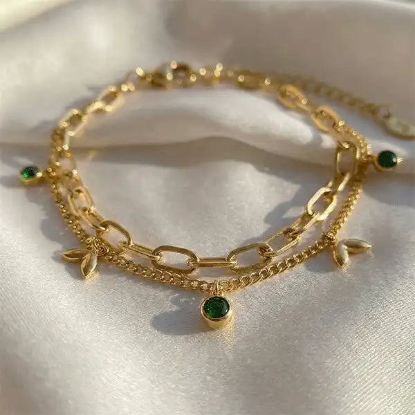 Gold anti-tarnish emerald charm bracelet with leaf details on white satin background