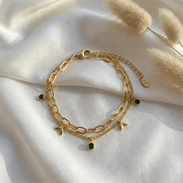 Flat lay of gold layered chain bracelet with green stone charms and leaf motifs, anti-tarnish jewellery
