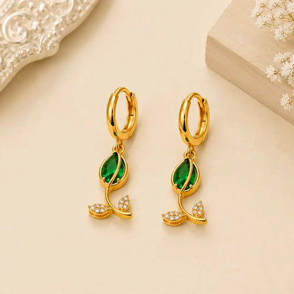 Pair of Emerald Petal anti tarnish hoop earrings with emerald green marquise-cut stones and crystal leaf motifs on a beige background.