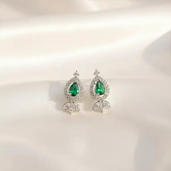 Emerald teardrop silver earrings placed on a soft neutral background with natural light