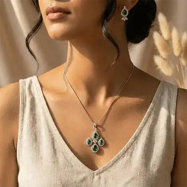 Emerald teardrop pendant necklace and earrings worn by model in soft sunlight, premium silver finish jewellery
