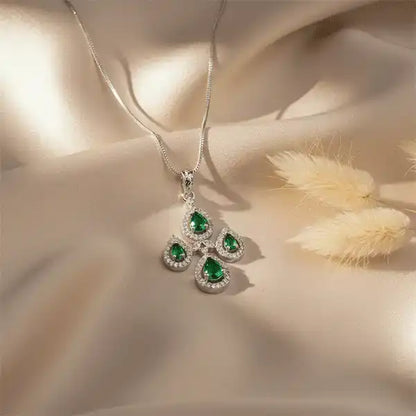 Emerald teardrop silver pendant necklace on beige satin fabric with pampas grass, minimal luxury jewellery