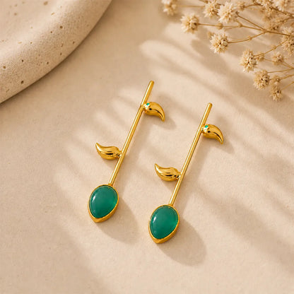 Pair of Emerald Vine anti tarnish brass earrings with emerald green teardrop stones and sleek gold-toned leaf motifs on a beige background.