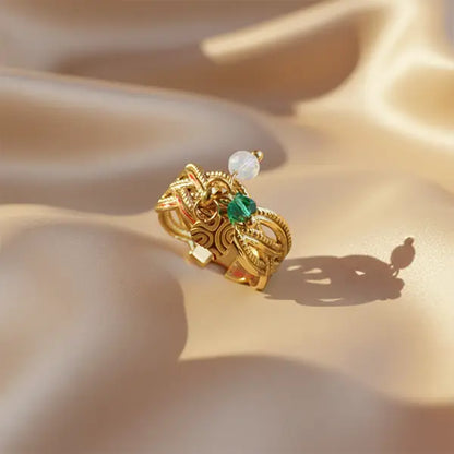 Ornate gold ring featuring detailed patterns and emerald-green charm resting on golden satin fabric with dramatic shadows.