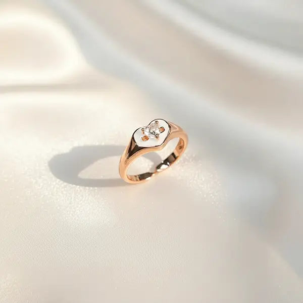 Rose gold heart-shaped ring with a central sparkling crystal displayed on soft satin fabric.