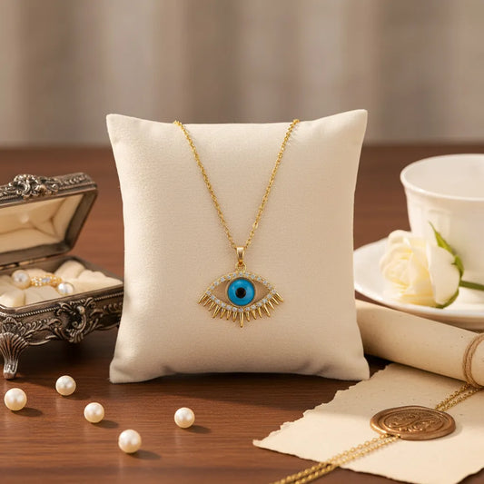 Gold Evil Eye pendant necklace with a turquoise blue center and crystal-studded lashes, resting on dried wheat stalks.