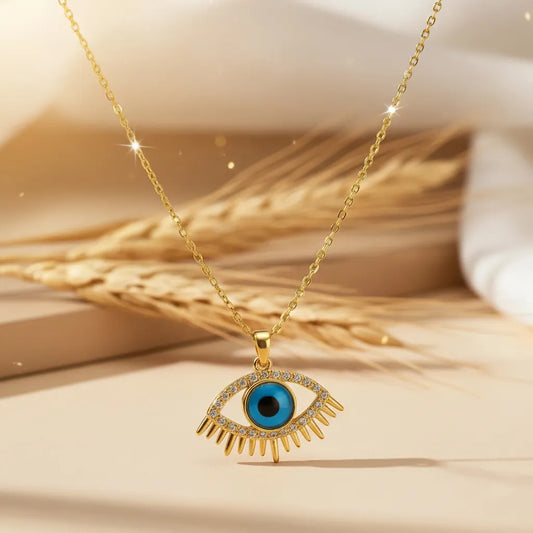 Gold Evil Eye pendant necklace with a turquoise blue center and crystal-studded lashes, resting on dried wheat stalks.
