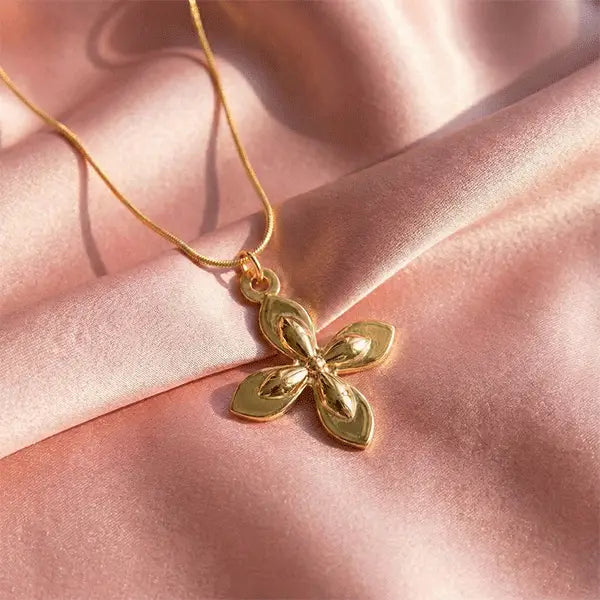 Gold flower pendant necklace displayed on soft pink satin under natural sunlight.