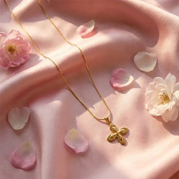 Gold floral pendant necklace styled on pink satin with rose petals and flowers for an elegant aesthetic.