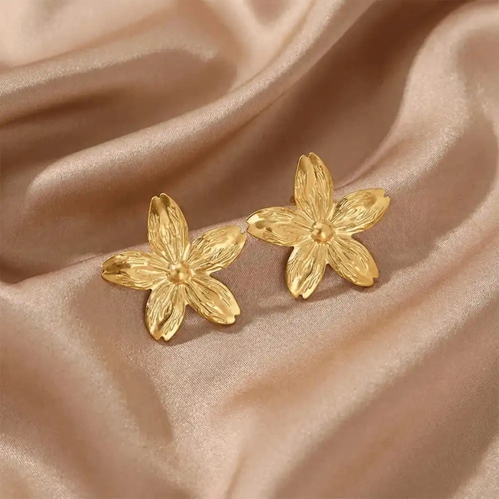 Anti-tarnish gold flower stud earrings placed on beige satin cloth, highlighting detailed petal design and glossy finish.