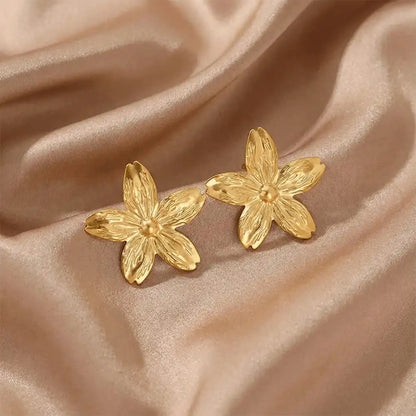 Anti-tarnish gold flower stud earrings placed on beige satin cloth, highlighting detailed petal design and glossy finish.