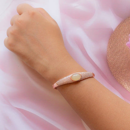 Glossy Rose gold bracelet with a central stone on a wrist against a soft pink background
