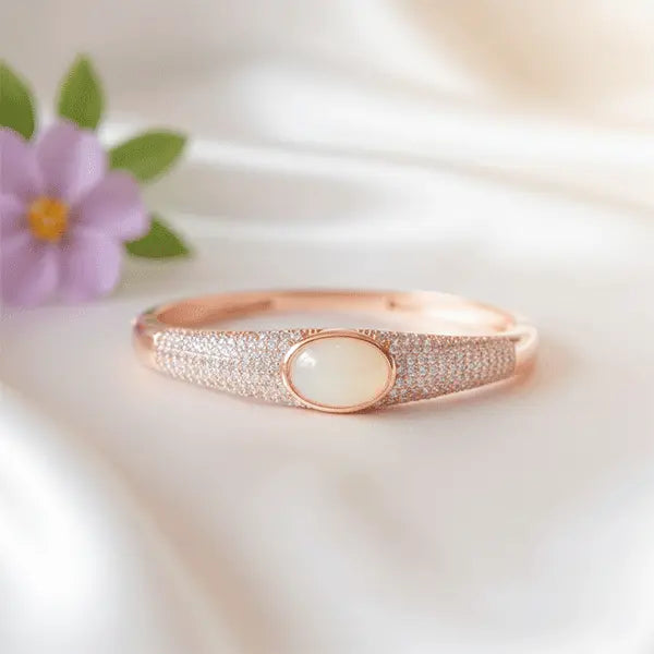 Glossy Rose gold bracelet with a central gemstone on a soft white fabric background
