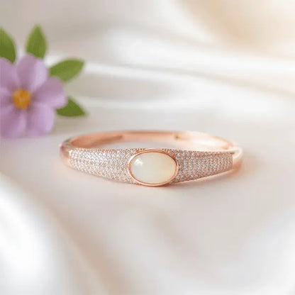 Glossy Rose gold bracelet with a central gemstone on a soft white fabric background