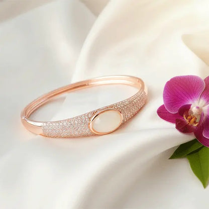 Glossy Rose gold bracelet with a white stone on a white fabric background with a purple orchid.