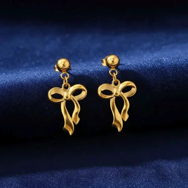 Gold Bow Drops earrings featuring a ribbon bow design showcased on deep blue velvet fabric.