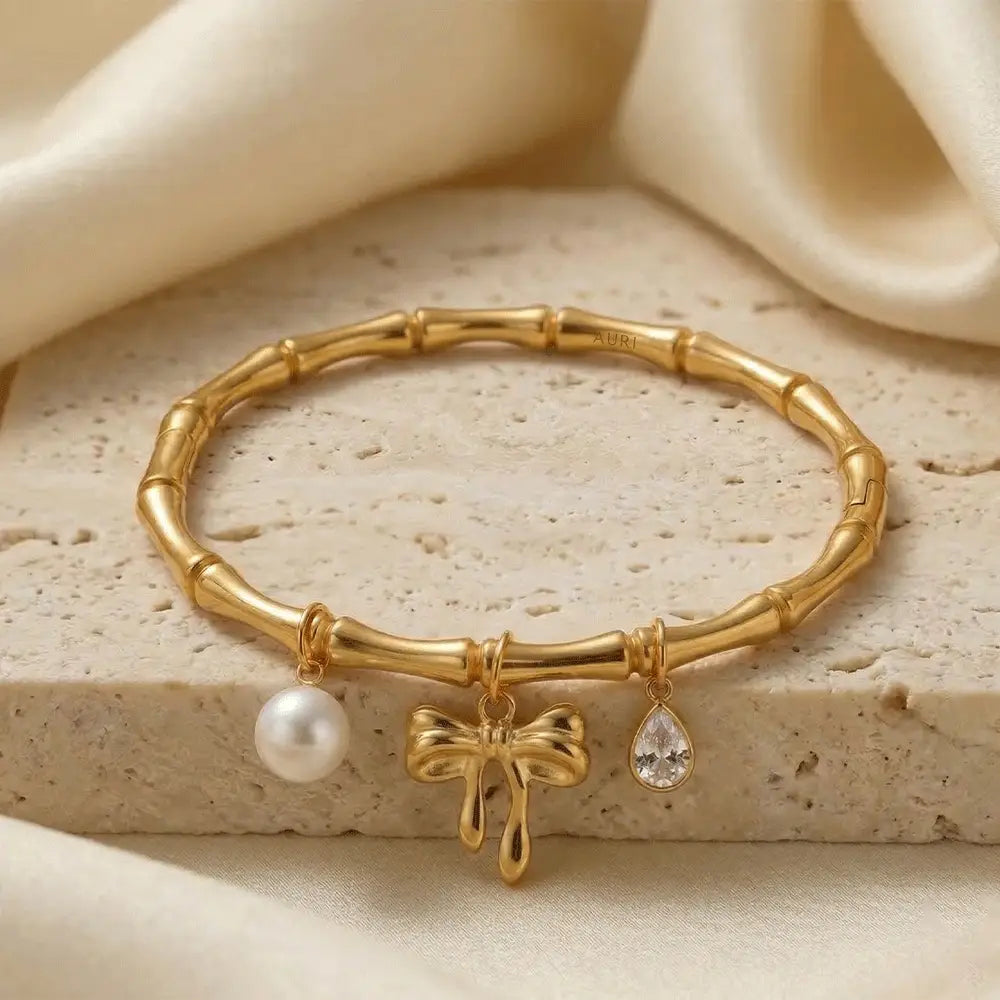 Elegant gold kada bracelet with pearl, bow charm, and teardrop crystal on textured stone with satin fabric, anti-tarnish jewellry