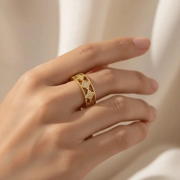 Gold Clover Band Ring with intricate clover pattern and crystals worn on hand against a beige backdrop.