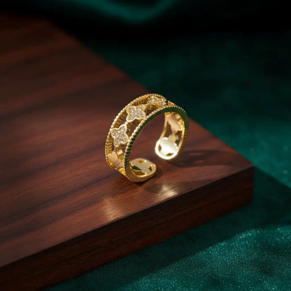 Gold Clover Band Ring with textured edges and crystal clover accents showcased on wooden block with dark green fabric.