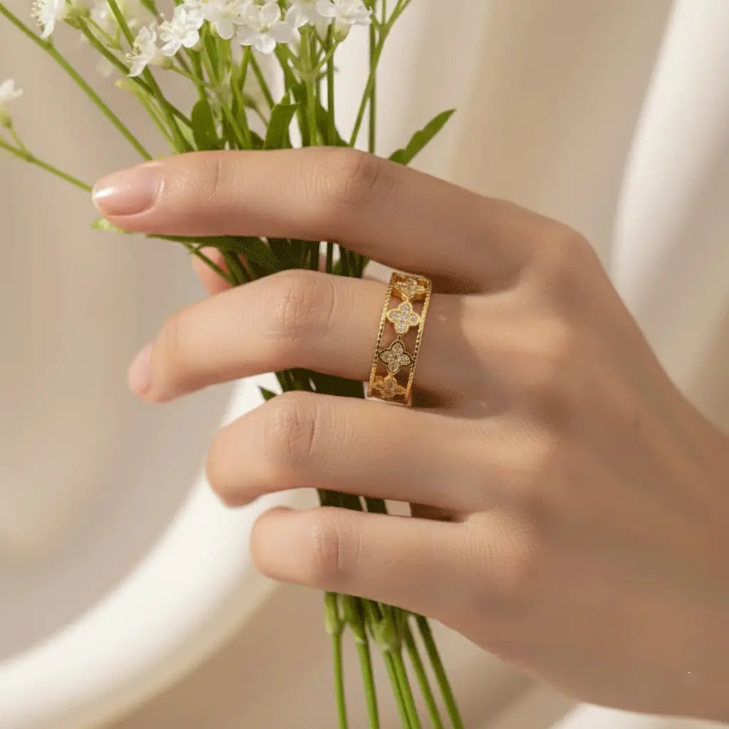Gold Clover Band Ring with cut-out clover motifs and crystal detailing worn on hand while holding white flowers.