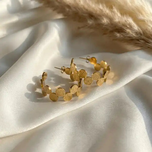 Gold Coin Hoops earrings in anti-tarnish gold finish styled on white satin fabric with soft sunlight