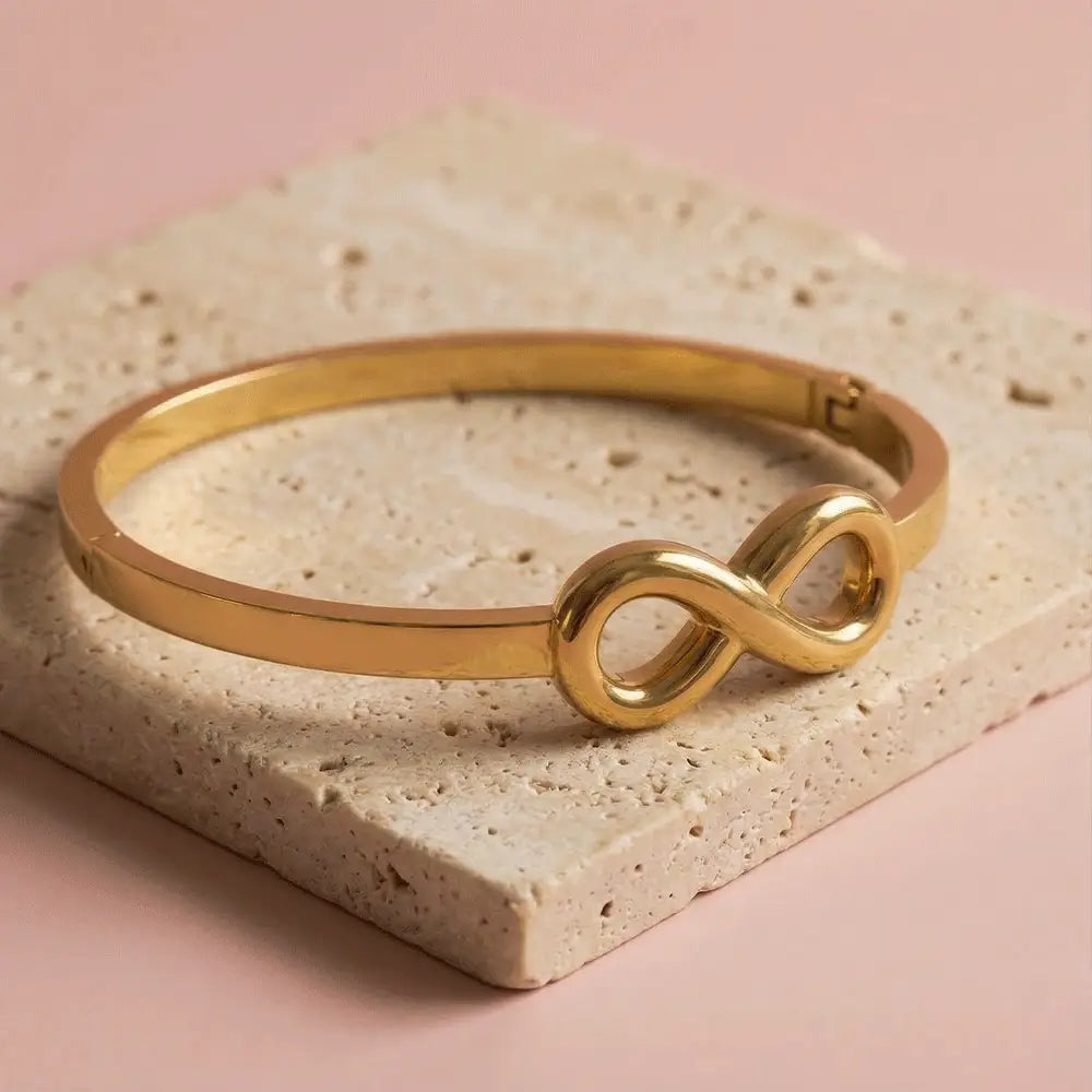 Minimal gold infinity kada bracelet on beige stone slab, sleek anti-tarnish bracelet for women, modern jewellry design