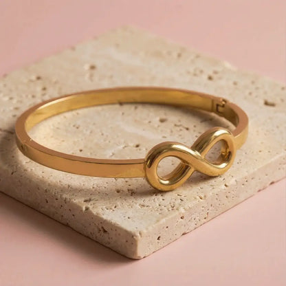 Minimal gold infinity kada bracelet on beige stone slab, sleek anti-tarnish bracelet for women, modern jewellry design