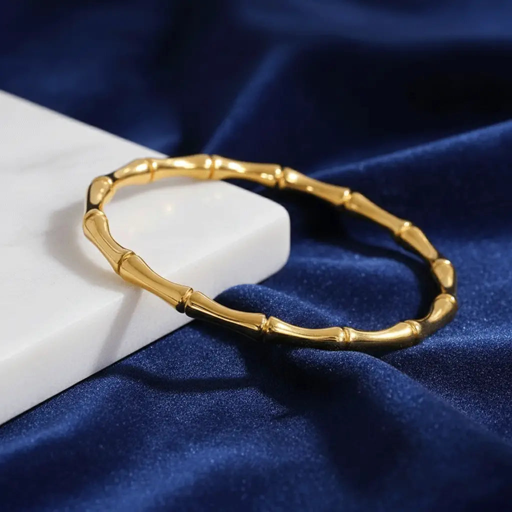 Shiny Gold Kada bracelet with bamboo-inspired structure placed on blue velvet fabric and white marble block.