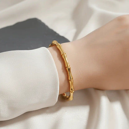 Gold Kada bracelet with bamboo-style design worn on wrist against a soft satin background.