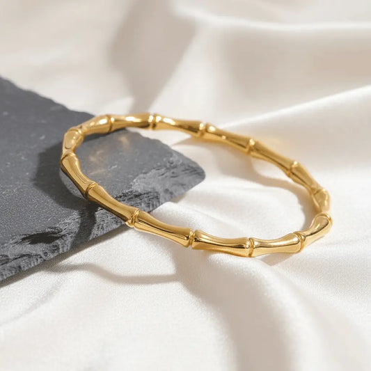 Elegant Gold Kada bracelet featuring bamboo-style segments displayed on white satin beside a dark stone tile.