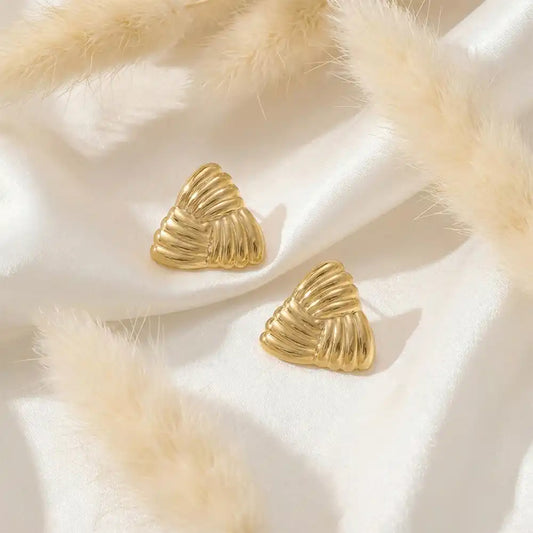 Anti-tarnish gold triangle stud earrings displayed on white satin fabric with pampas grass for a minimal luxury look.