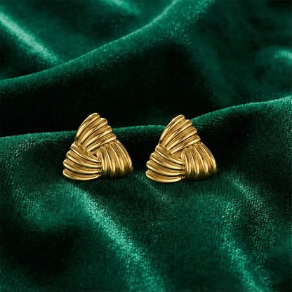 Gold triangle stud earrings placed on rich green velvet fabric, highlighting the ribbed texture and polished gold shine.