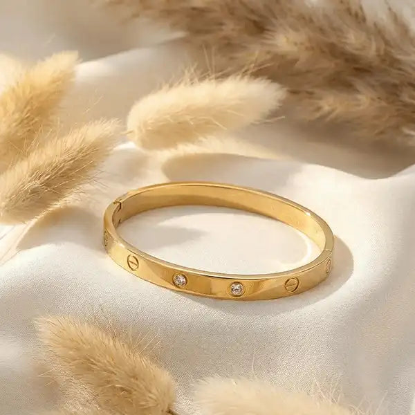 Gold anti-tarnish screw design bangle placed on white satin fabric with pampas grass, elegant jewellery product photography