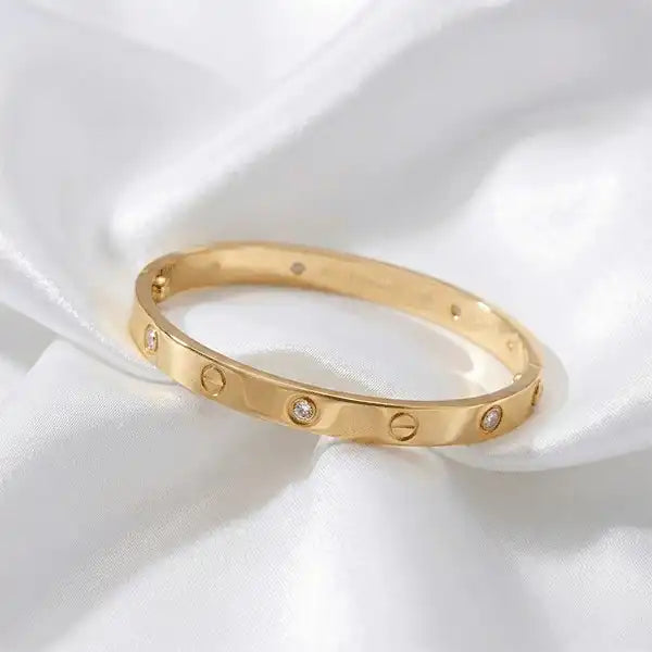 Close-up of gold anti-tarnish bangle with crystal screw details on white satin background, premium jewellery studio shot