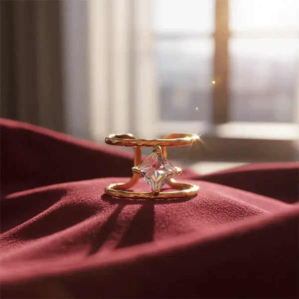 Gold double-band ring with a floating square-cut crystal showcased on rich maroon fabric under warm sunlight.