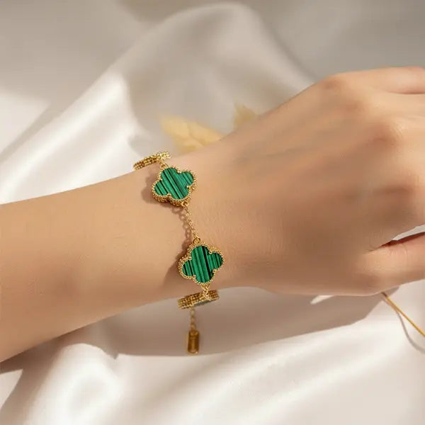 Hand wearing a green clover four-leaf charm bracelet with gold detailing on a satin background.