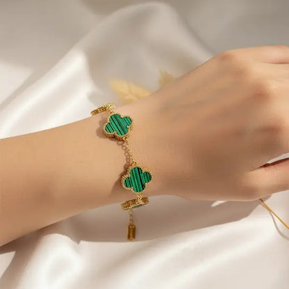 Hand wearing a green clover four-leaf charm bracelet with gold detailing on a satin background.