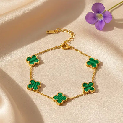 Gold chain bracelet featuring green clover charms with malachite texture, styled on beige satin with a purple flower.