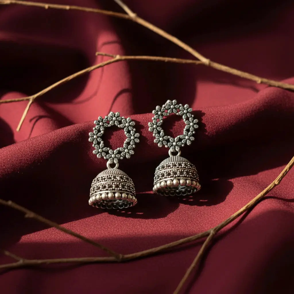 Intricate oxidised silver Gulzar Jhumka earrings displayed on rich maroon fabric with soft natural light.