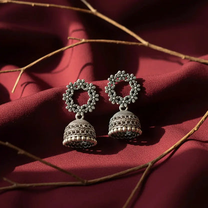 Intricate oxidised silver Gulzar Jhumka earrings displayed on rich maroon fabric with soft natural light.