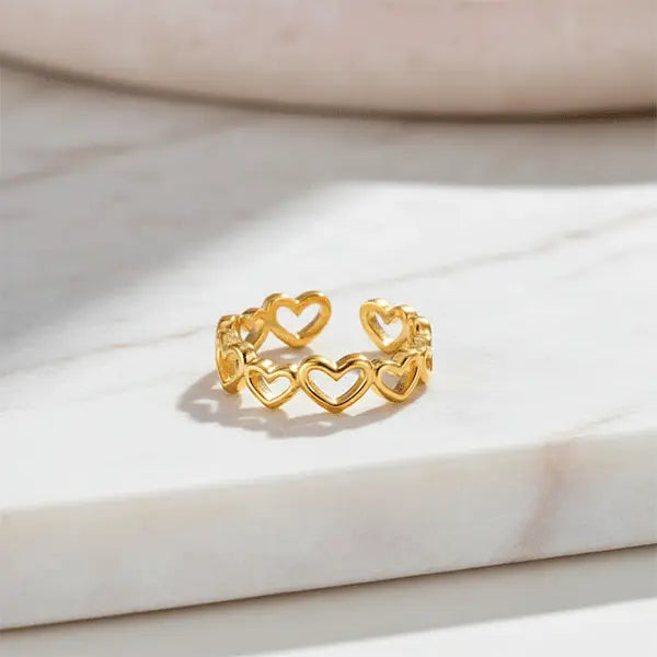 Gold open-heart band ring displayed on a white marble surface under natural sunlight.