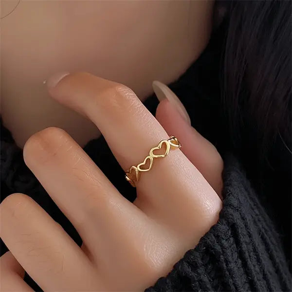 Gold heart-shaped band ring worn on a woman’s hand with a black sweater, close-up view.