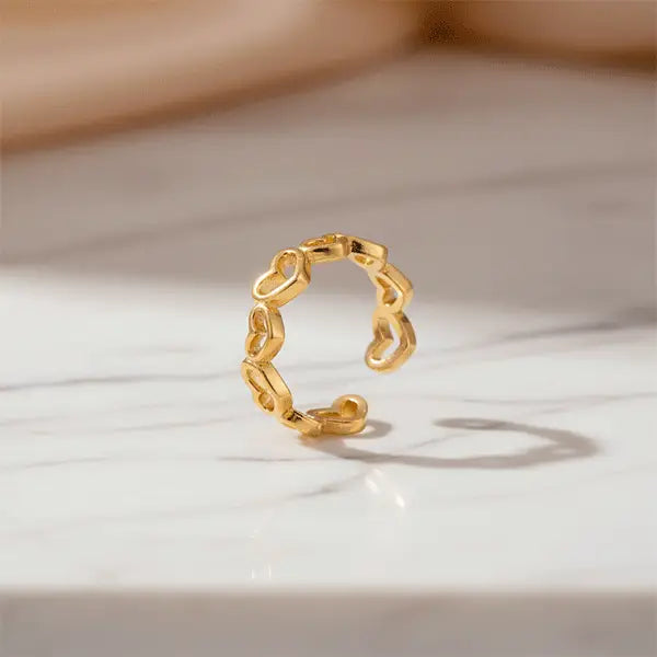 Gold open-heart ring standing upright on a marble surface with soft shadows.